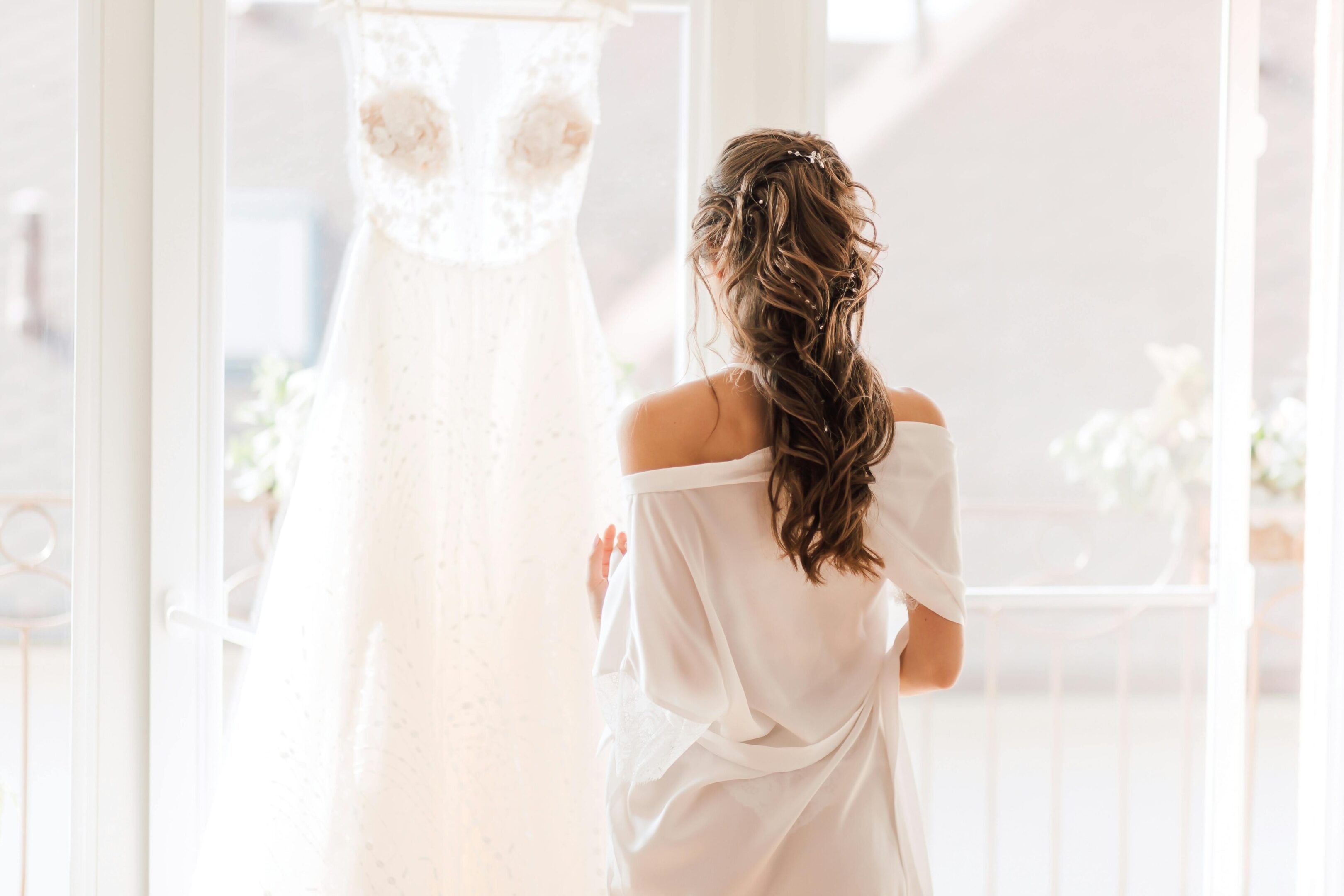 A woman in white dress standing next to a wedding gown.