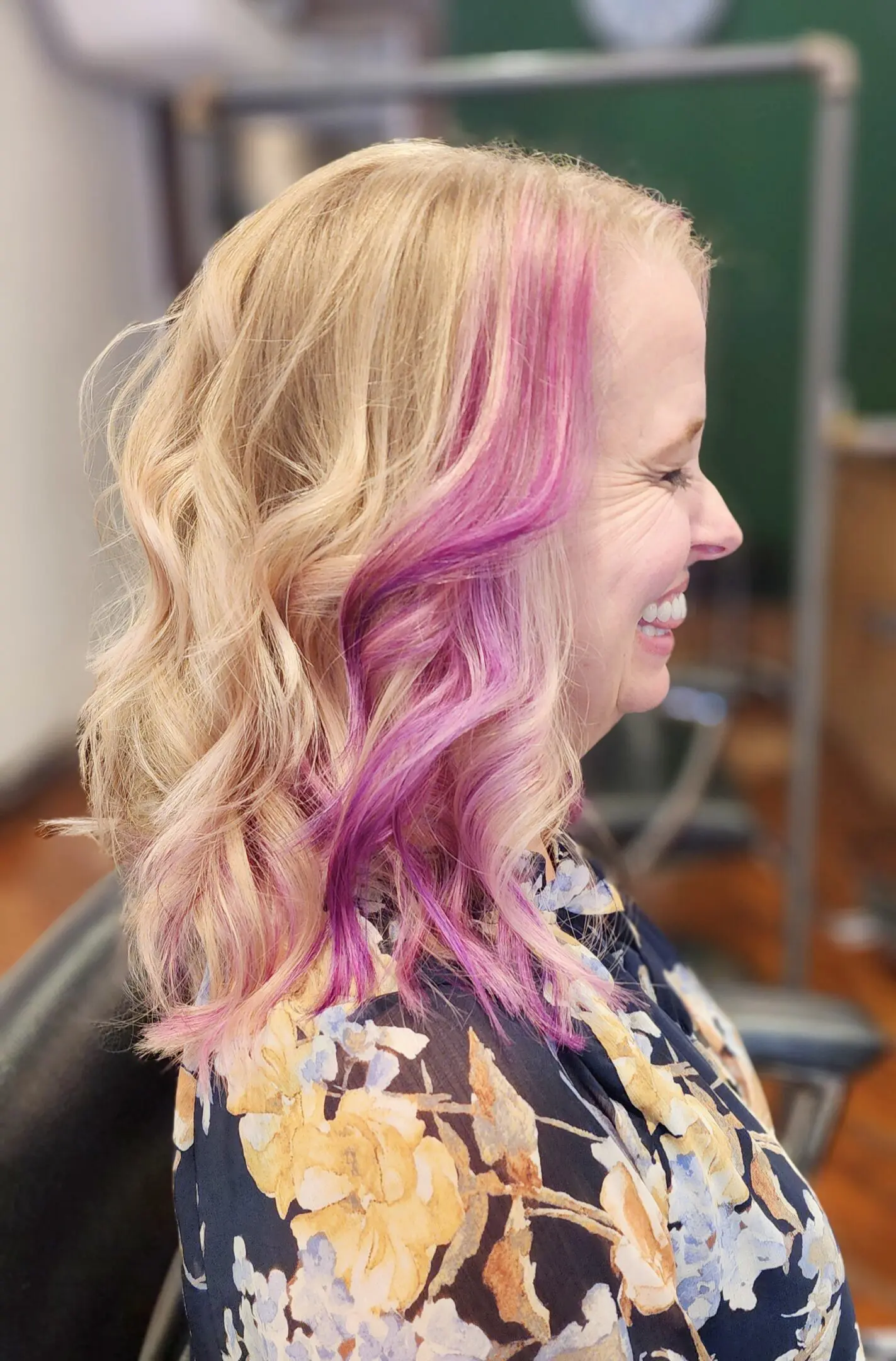 A woman with pink hair in front of a mirror.