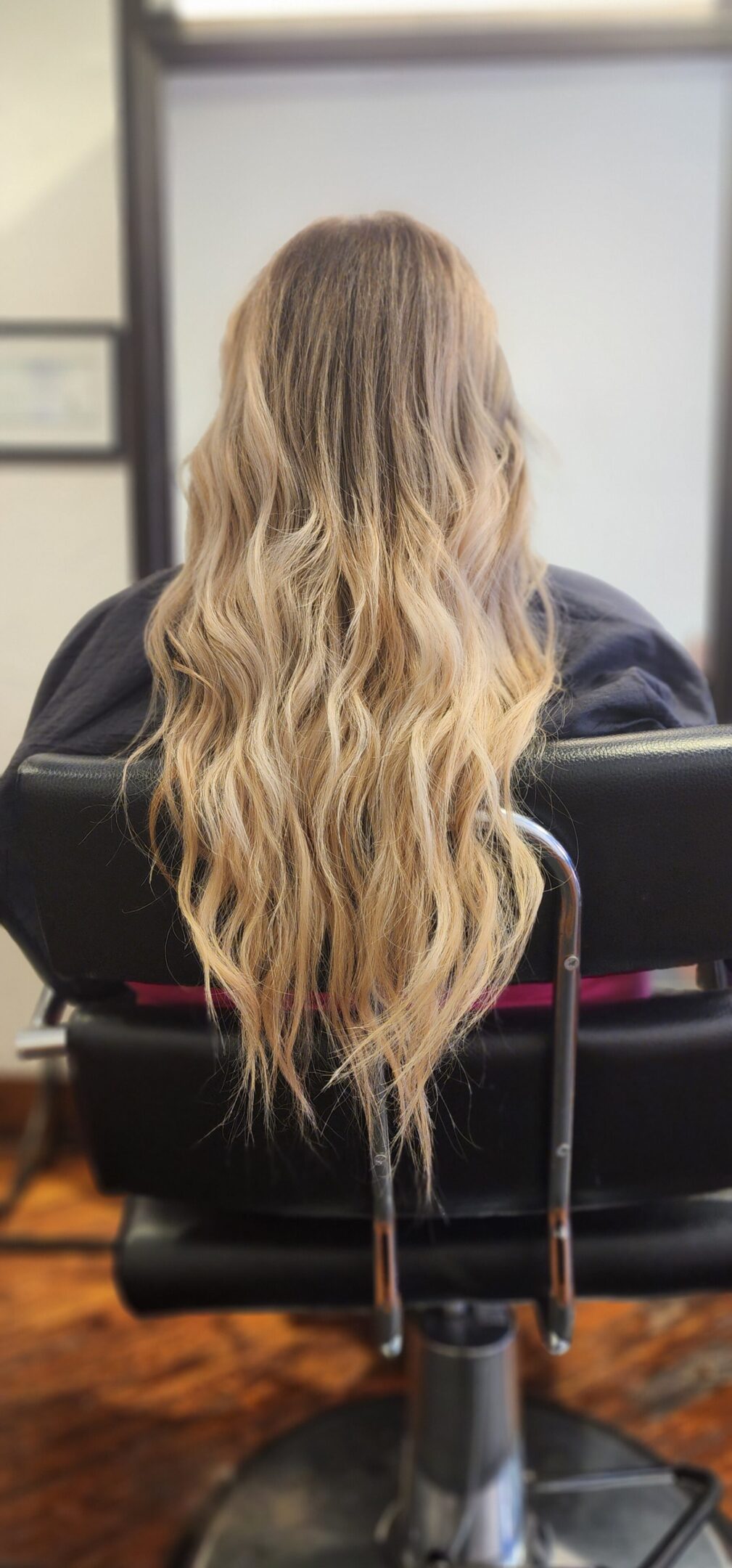 A woman sitting in front of a mirror with long blonde hair.