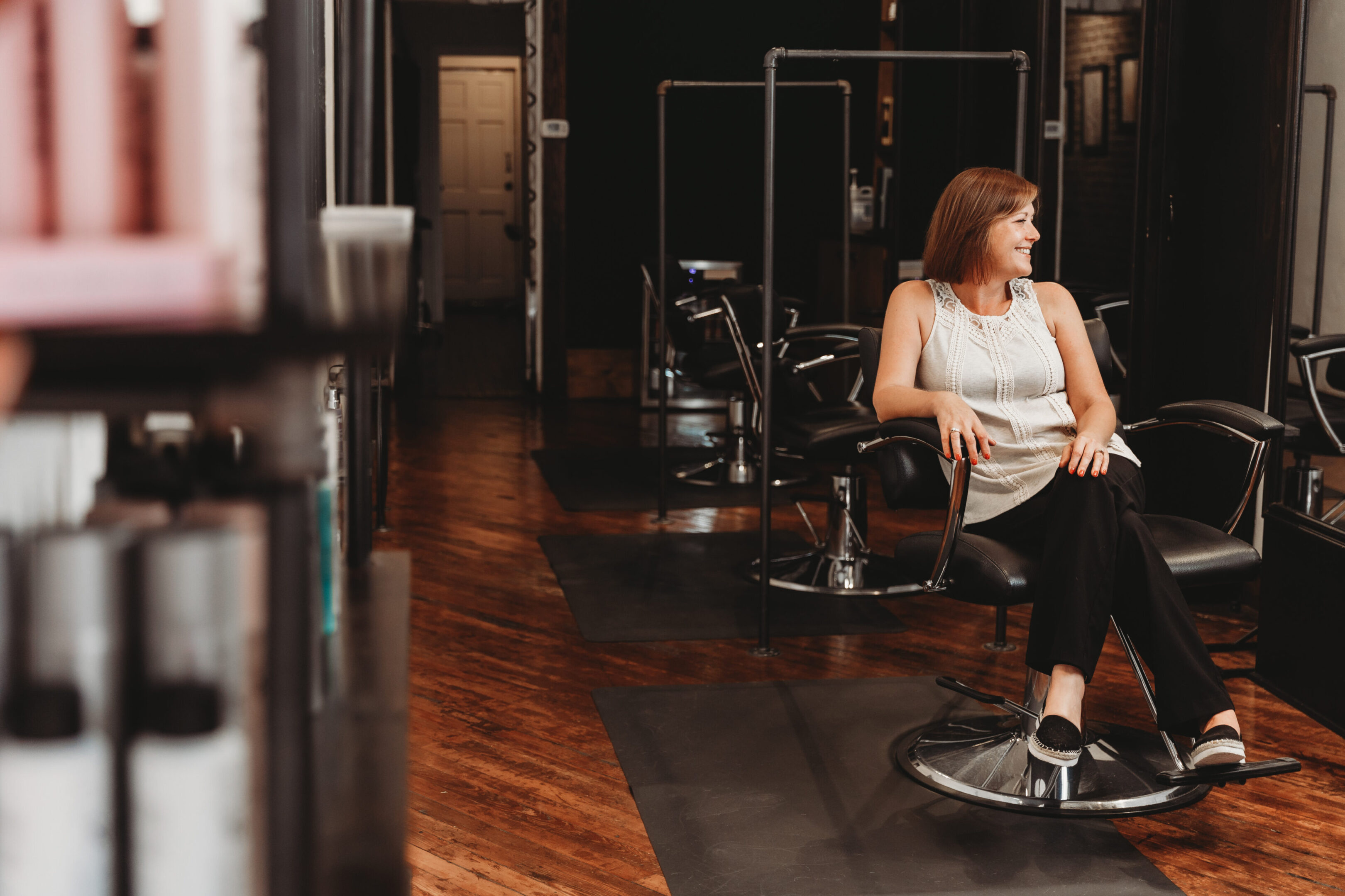 A woman sitting on top of a chair in front of some hair dryers.